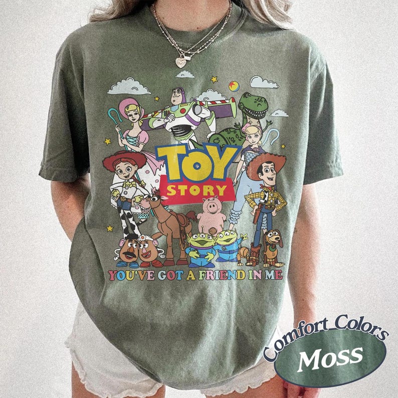 以下が含まれることがあります： モスグリーンのTシャツ。アニメ映画「トイ・ストーリー」のキャラクターのカラフルなグラフィックが特徴です。デザインにはウッディ、バズ・ライトイヤー、その他のキャラクターが含まれており、「TOY STORY」と「YOU'VE GOT A FRIEND IN ME」の文字があります。