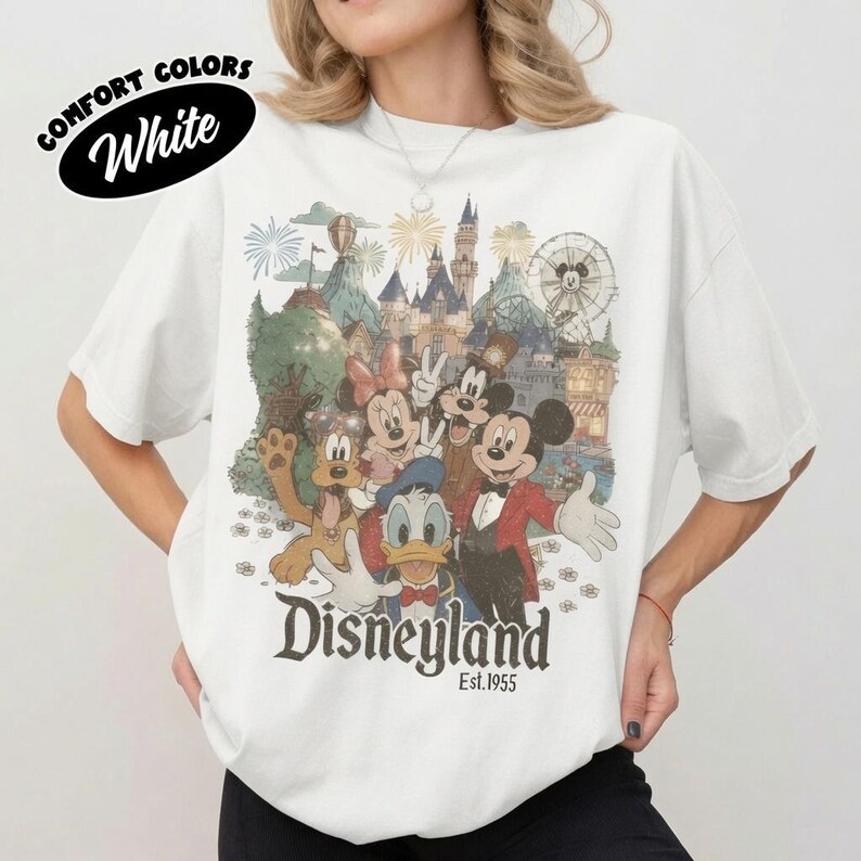 May include: A white t-shirt featuring a vintage-style graphic of Mickey Mouse, Minnie Mouse, Donald Duck, and Pluto in front of a castle and Ferris wheel. The text "Disneyland" and "Est. 1955" is printed below the characters in a dark serif font.
