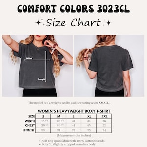 May include: A dark gray Comfort Colors 3023CL women's heavyweight boxy t-shirt. The image includes a size chart with measurements in inches for sizes S to 2XL. The shirt is made of soft ring spun fabric with 100% cotton threads.