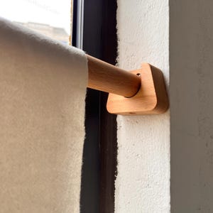 May include: A wooden towel rail with a light-coloured towel. The rail is made of light-coloured wood and is mounted on a white wall. The towel is a light cream colour and is hanging from the wooden rod.