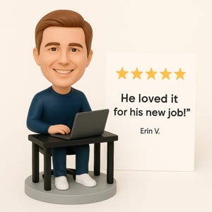 May include: A bobblehead figurine of a man sitting at a small black desk with a laptop. The man is wearing a blue shirt and pants, and white sneakers. A sign with five gold stars and the text "He loved it for his new job!" is next to the figurine.