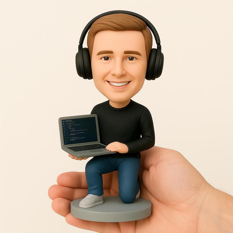May include: A figurine of a smiling person wearing headphones, black long-sleeve shirt, and blue jeans, kneeling on a gray base. The figurine holds a gray laptop displaying code. The figurine is being held in a hand.