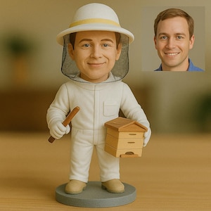 Puede incluir: Figura de apicultor con traje, sombrero y velo blancos, sosteniendo una colmena de madera y un palo. Una imagen más pequeña de la cara de un hombre está en el fondo. La figura está sobre una base circular gris.