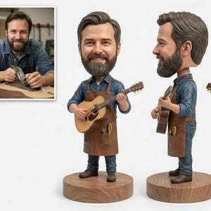 May include: A bobblehead figurine of a man playing an acoustic guitar. The figure is wearing a denim shirt, brown apron, and blue jeans. The base is a round, wooden platform. A framed photo of a man working on a guitar is in the background.
