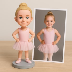 May include: A figurine of a young ballerina in a pink leotard and tutu, with a matching photo. The figurine has blonde hair in a bun and is standing on a gray base. The photo shows a young girl in a similar outfit.