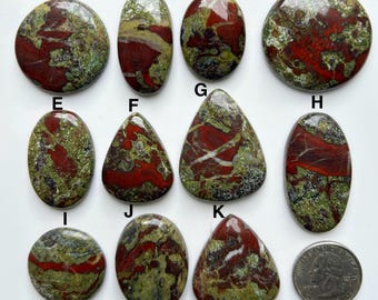 May include: A collection of eleven polished dragon blood jasper gemstones in various shapes, including oval, round, and teardrop. The stones display a mix of deep red and green hues, with some featuring white veining. A quarter coin is included for size reference.