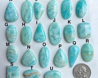 May include: A selection of twenty-one polished Amazonite gemstones in diverse shapes, such as teardrop, oval, and rectangular. The stones exhibit blue-green shades with white veining. A UK coin is included for size reference.