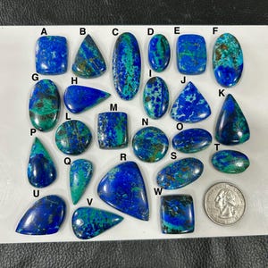 May include: A selection of azurite gemstones in diverse forms, such as oval, rectangular, and teardrop. The stones exhibit a vivid blue hue with green veining. A coin is included for size comparison.