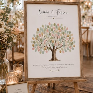 Puede incluir: Un libro de visitas de boda con árbol de huellas en un marco de madera sobre un caballete. La lámina muestra un árbol con hojas de huellas dactilares de colores, el texto Leonie & Fabian, 25 septiembre 2026 y Rooted in love, surrounded by those.