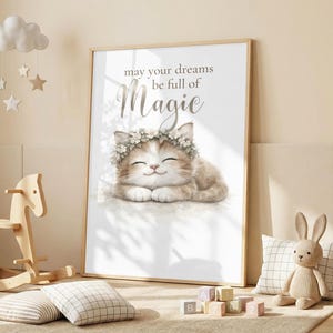 以下が含まれることがあります： 花冠をつけた笑顔の子猫の水彩イラストが描かれたフレームプリント。子猫の上には「may your dreams be full of Magic」という文字が書かれています。プリントは明るい色の木製フレームに入っています。