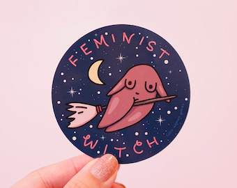 Puede incluir: Una pegatina circular con fondo azul oscuro que muestra una figura rosa abstracta con pechos montada en una escoba. El texto FEMINIST WITCH está impreso en rosa alrededor de los bordes, junto a una luna creciente amarilla y estrellas blancas.