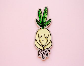 May include: A die-cut sticker featuring a stylized, pale yellow root vegetable character with a human-like torso, two small breasts, and a sad facial expression. The character has three bright green leaves on top and dark brown roots at the base.
