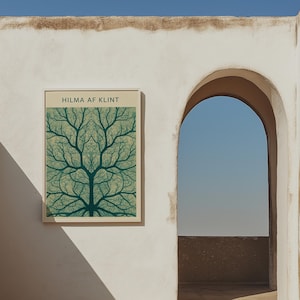 Könnte beinhalten: Ein gerahmter Kunstdruck mit einem symmetrischen Baumdesign in Türkis- und Grüntönen. Der Druck trägt oben die Aufschrift "HILMA AF KLINT". Das Kunstwerk hängt an einer weißen Wand neben einem bogenförmigen Tor, durch dessen Öffnung ein klarer blauer Himmel zu sehen ist.