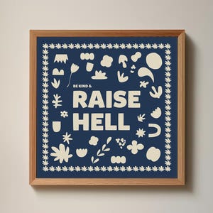 Könnte beinhalten: Ein gerahmter Kunstdruck mit marineblauem Hintergrund und den Worten "BE KIND & RAISE HELL" in Weiß. Der Druck zeigt verschiedene cremefarbene Blumen- und abstrakte Formen, gerahmt in einem hellbraunen Holzrahmen.