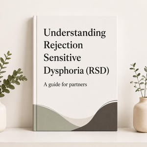 May include: A hardcover book with a white cover featuring the black text Understanding Rejection Sensitive Dysphoria (RSD) A guide for partners. The bottom of the cover has abstract wavy shapes in muted sage green, light gray, and dark charcoal.