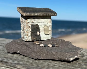 Casa de playa en miniatura de madera a la deriva con ventana de cristal de playa.