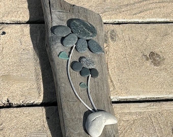 Arte floral con piedras negras sobre madera flotante: decoración playera del lago Michigan.