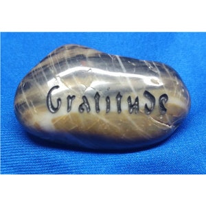 May include: A smooth, gray and white stone with the word "Gratitude" engraved in black lettering.