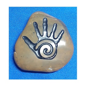 May include: A hand-painted stone with a black handprint and a spiral design. The stone is a light brown color.