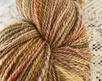 May include: A skein of yarn in shades of brown, beige, and orange. The yarn is hand-spun and has a rustic, natural look.
