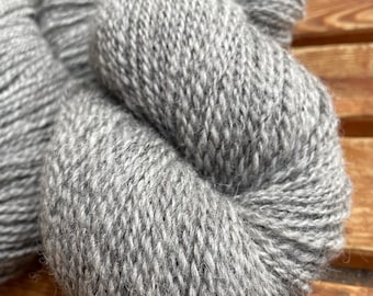 May include: Close-up of several skeins of gray yarn. The yarn is thick and textured, with a slightly fuzzy appearance. The color is a medium gray, and the yarn appears to be made of a natural fiber. The skeins are arranged in a loose, organic shape.