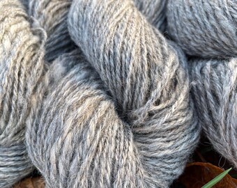 May include: Close-up of several skeins of gray yarn. The yarn appears to be thick and textured, with variations in color from light to dark gray. The yarn is tightly wound, suggesting it is ready for use in knitting or other fiber crafts.
