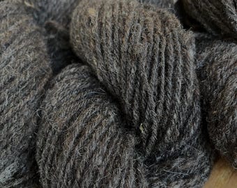 May include: A collection of dark brown, textured yarn skeins with a visible wool fiber composition. The yarn features a multi-ply twisted structure with a matte finish and natural color variations throughout the fibers, showing a dense, fuzzy surface.