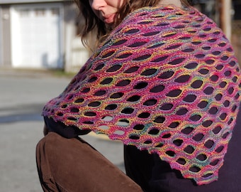 May include: A colorful, open-weave shawl in shades of pink, purple, yellow, and green. The knitted accessory features a repeating oval pattern, creating a delicate, airy design. The shawl is draped over the shoulders, showcasing its vibrant color palette and texture.