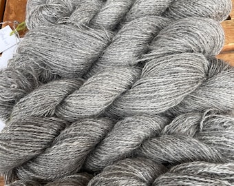 May include: A large, thick skein of heathered gray yarn with a twisted, multi-ply texture. The yarn displays a blend of light and dark gray fibers, creating a variegated appearance throughout the entire length of the twisted wool strands.