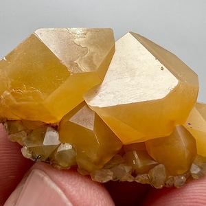 Könnte beinhalten: Ein Cluster aus goldgelben Quarzkristallen mit scharfen, geometrischen Formen. Die Kristalle haben eine warme, durchscheinende Farbe und ruhen auf einer Basis aus kleineren, helleren Kristallen. Das Gesamtbild ist natürlich und mineralisch.