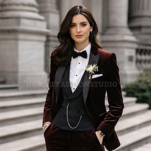 May include: A burgundy velvet suit with a black lapel, bow tie, and vest. The suit includes a white dress shirt and a pocket square with a flower. The watch and chain add a touch of elegance. The suit is a formal wear ensemble.