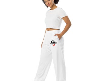 May include: White athletic pants with a wide leg and a small logo on the left pocket. The logo is black and red. The pants are paired with a white crop top. The model is wearing white sneakers.