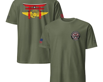 May include: Olive green t-shirts with military-themed graphics. One shirt features a red Torii gate and a golden emblem on the back. The other shirt has a circular patch with a military design on the front.