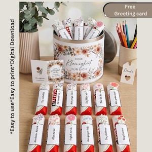 May include: A cylindrical metal tin decorated with floral patterns and the text Eine Kleinigkeit für dich, filled with chocolate bars wrapped in white labels with floral illustrations and German phrases. Includes a matching greeting card and pencils.