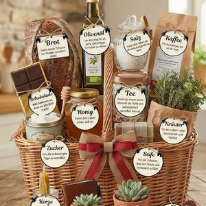 May include: A woven wicker gift basket filled with assorted items including a loaf of bread, olive oil, salt, coffee, chocolate, honey, tea, herbs, sugar, soap, a candle, a notebook, succulents, and keys. Each item features a round white tag with German text.