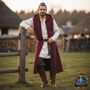 Puede incluir: Un chaleco con capucha burdeos con un diseño largo y fluido, usado sobre una túnica color crema y pantalones marrones. El atuendo incluye un cinturón y botas de cuero marrón. La imagen muestra a una persona apoyada en una valla de madera en un campo de hierba.