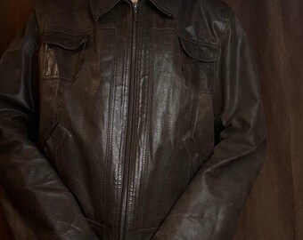 Könnte beinhalten: Dunkelbraune Lederjacke mit Reißverschluss, zwei Brusttaschen und Kragen. Die Jacke hat ein leicht abgenutztes Aussehen und lange Ärmel. Die Jacke ist mittelschwer und scheint Vintage zu sein.
