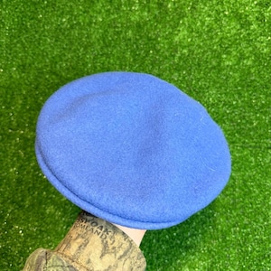 K&ouml;nnte beinhalten: Ein einfarbiger blauer Barett-Hut. Der Hut besteht aus einem weichen, filzartigen Material. Der Hut ist ein klassischer Stil, der f&uuml;r verschiedene Anl&auml;sse geeignet ist. Der Hut hat einen leuchtenden Blauton.