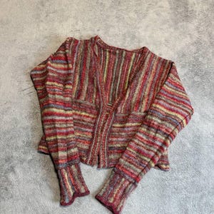May include: A long-sleeved cardigan featuring a multi-colored striped pattern in shades of red, yellow, blue, and purple. The knit garment has a V-neckline, a front opening, and fitted cuffs with a slightly flared, wavy edge at the wrists.