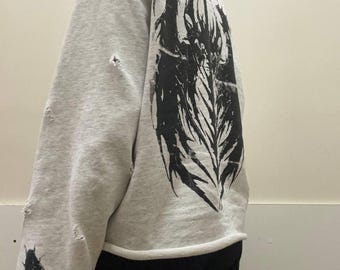 May include: A light gray sweatshirt with distressed details and a large black graphic on the back. The sleeve features a small insect graphic and the text "ESSENTIALS FEAR OF GOD".