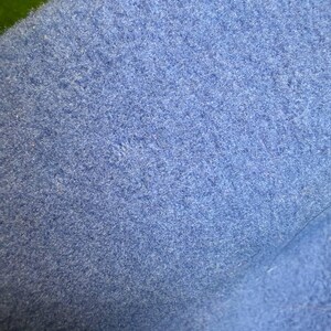 K&ouml;nnte beinhalten: Nahaufnahme eines strukturierten, hellblauen Stoffes. Das Material scheint eine weiche Wolle oder Filz zu sein, mit einer leicht unebenen Oberfl&auml;che. Die Farbe ist ein ged&auml;mpftes, pastellblau, und die Textur ist dicht und leicht flauschig.