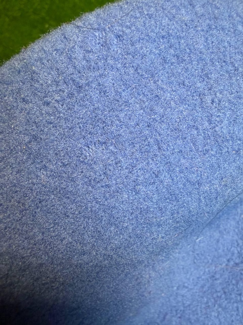 K&ouml;nnte beinhalten: Nahaufnahme eines strukturierten, hellblauen Stoffes. Das Material scheint eine weiche Wolle oder Filz zu sein, mit einer leicht unebenen Oberfl&auml;che. Die Farbe ist ein ged&auml;mpftes, pastellblau, und die Textur ist dicht und leicht flauschig.