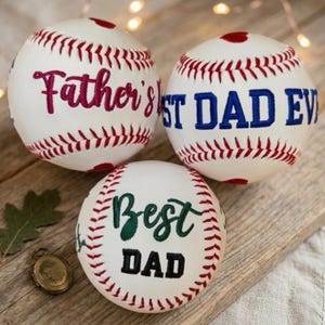 Puede incluir: Tres pelotas de béisbol blancas con costuras rojas y texto. Una dice "Father's" en magenta, otra "ST DAD EV" en azul y la tercera "Best DAD" en verde y negro.