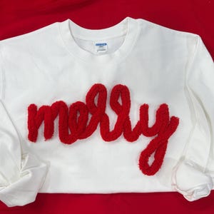 May include: A white sweatshirt with the name "molly" in red, textured lettering across the chest. The long-sleeved shirt is displayed on a red surface.