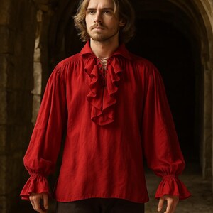 May include: A red long-sleeve shirt with a ruffled front and cuffs. The shirt has a lace-up neckline and is made of a soft fabric. The sleeves are long and gathered at the wrists. The shirt is a historical or renaissance style.