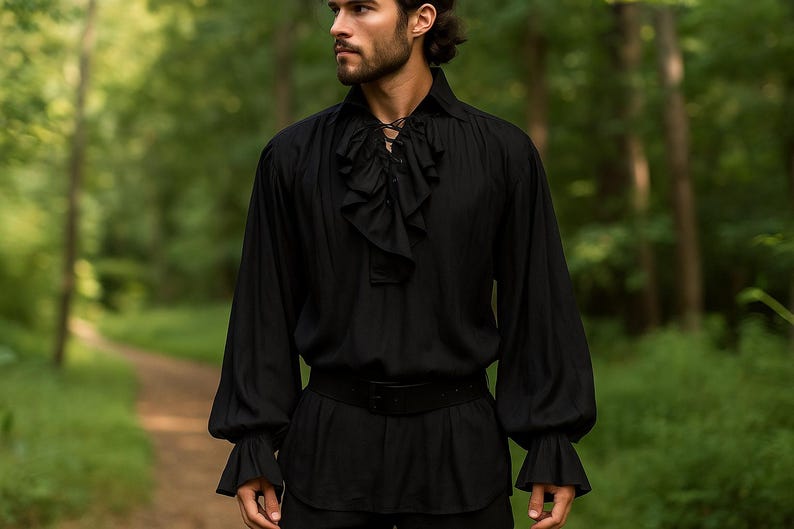 May include: Black long-sleeve shirt with a ruffled front and cuffs. The shirt has a lace-up neckline and is paired with a black belt. The image is set against a blurred green background.