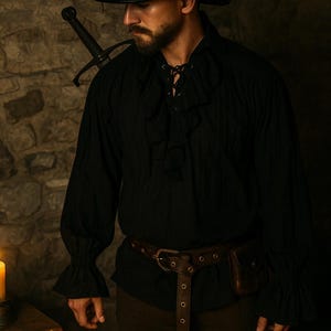 May include: Black long-sleeved shirt with ruffled cuffs and a lace-up neckline. A brown leather belt with a pouch is worn around the waist. A sword is over the shoulder. A lit candle and scroll are on a wooden table.