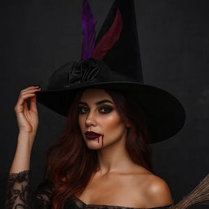 以下が含まれることがあります： 紫とバーガンディの羽が付いた黒い魔女の帽子。女性は黒いオフショルダーのドレスを着ており、顎には血のような汚れが付いた濃いメイクをしています。背景にはほうきがあります。ハロウィーンをテーマにしています。
