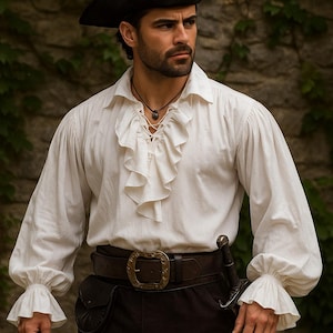 May include: A white pirate shirt with ruffled detailing on the front and cuffs. The shirt has long sleeves and is paired with a dark brown belt with a large buckle, black pants, and a black hat. A sword is attached to the belt.