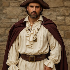 May include: A person wearing a historical costume. The outfit includes a brown hat, a cream-colored ruffled shirt, a brown cape, and a brown belt with a square buckle. The background is a stone wall.